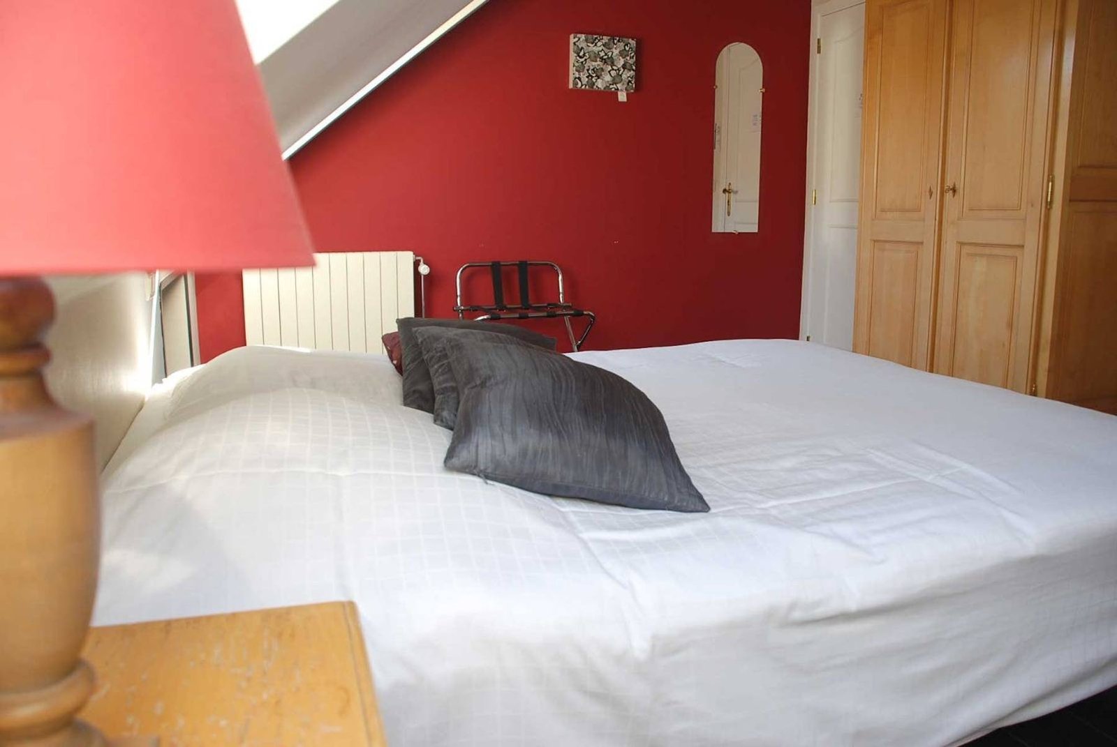 Chambre au mur rouge, grand lit blanc et coussins gris
